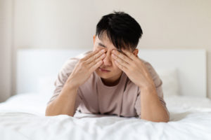 Homme asiatique endormi allongé sur le lit, se frottant les yeux